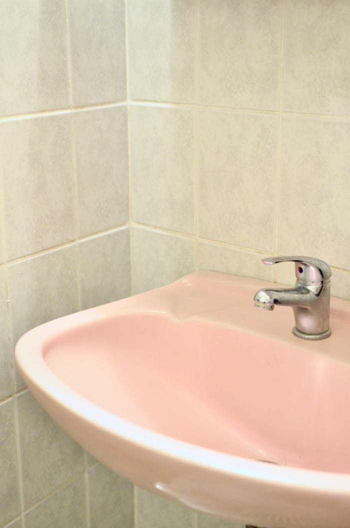 Pink sink with faucet placed at corner of bathroom with tiled wall in room during daily hygiene routine in flat