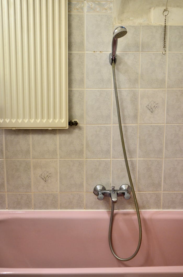 A vintage-style bathroom with a pink bathtub, silver shower head, and patterned tiles.